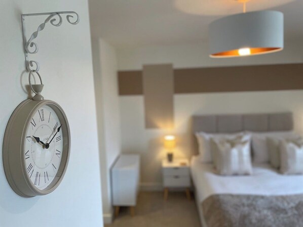 A bedroom with a bed, a nightstand, a wall-mounted clock, and a hanging light fixture.