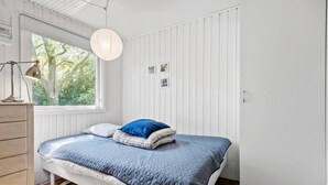 Een slaapkamer met een bed, een dressoir, een raam met uitzicht op bomen en een hanglamp.
