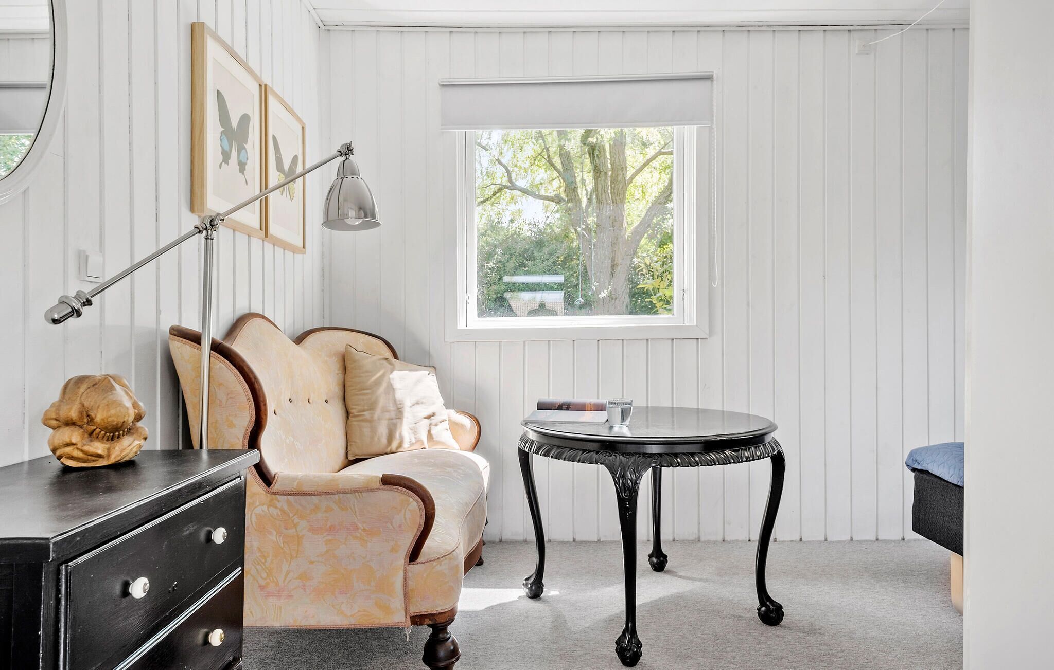 Ein Zimmer mit einer Couch, einem kleinen runden Tisch, einer Lampe und einem Fenster mit Blick auf Bäume.