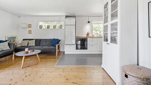 Een moderne woonkamer met een grijze bank, een ronde salontafel en een keuken met witte kasten en een inbouwoven.