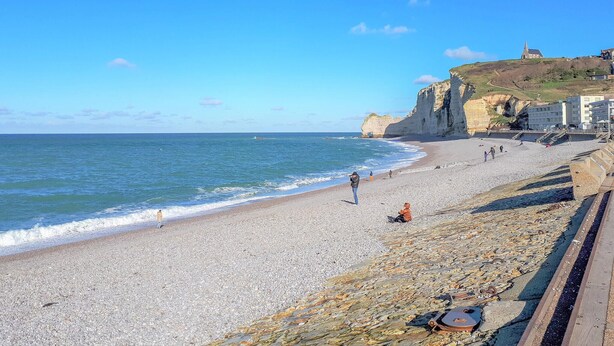 Une plage de galets, avec une falaise et une église située sur une colline.