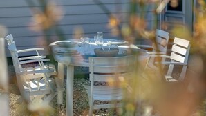 Une table de salle à manger ronde, entourée de chaises blanches, mise avec des assiettes, des verres et un saladier.