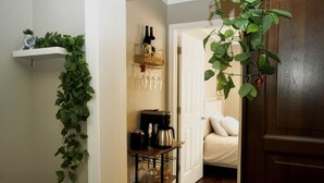 A hallway with a white door, a bed with white bedding, a coffee machine, and a shelf with wine bottles and glasses. - Luxurious 3-Level Home Minutes from Washington D.C. (Arlington)