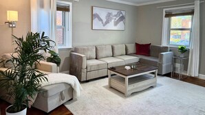 A living room with a beige sectional sofa, a coffee table, a ceiling fan, and a large window with curtains. - Luxurious 3-Level Home Minutes from Washington D.C. (Arlington)