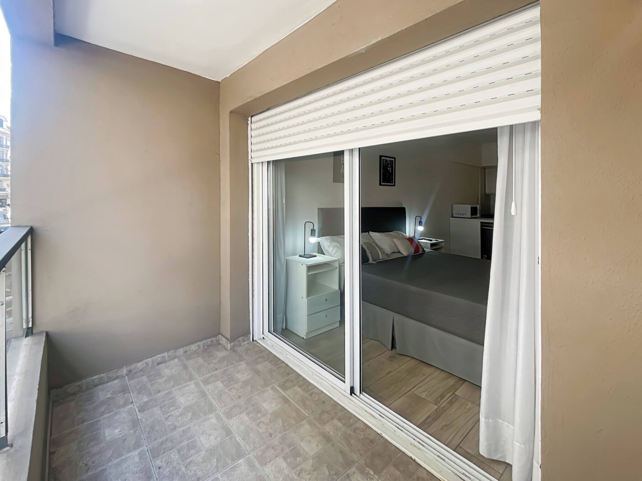 Habitación de hotel con puerta de vidrio corrediza que da a un balcón, una cama con almohadas, una mesita de noche y una lámpara.