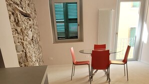 Un salon moderne avec un mur d’accent en pierre, un coin repas avec des chaises rouges et une grande fenêtre avec des stores.