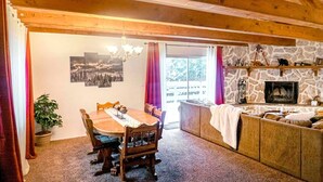 A cozy dining area with a wooden table and chairs, a stone fireplace, and a view of the outdoors. - Walk to Bear Mountain-Rustic 3bd sleeps 9 Hot Tub and Fire Pit~0.2 Miles to Bear Mountain (Big Bear Lake)