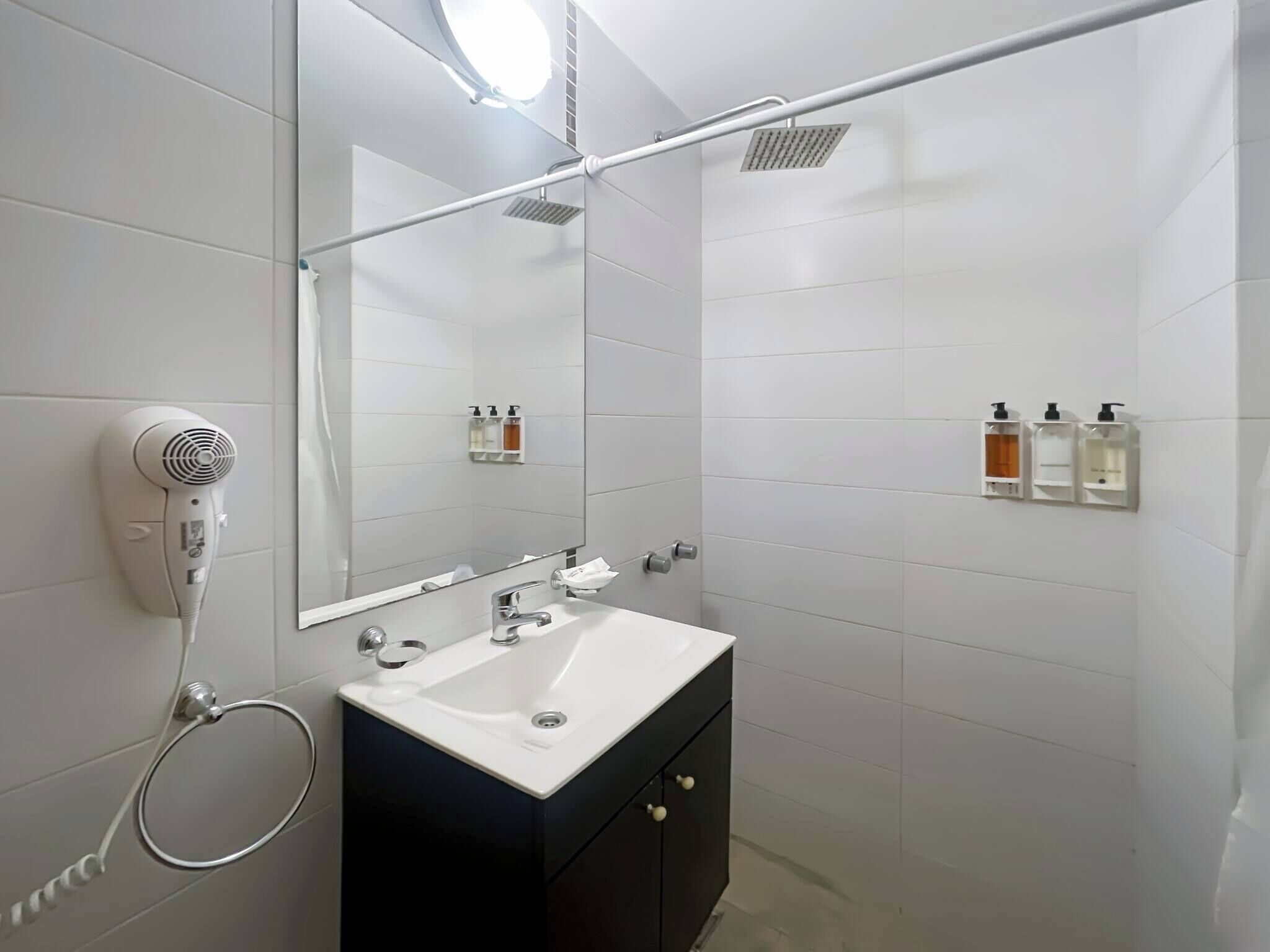 Ein modernes Badezimmer mit einem weißen Waschbecken, einem Spiegel und einem an der Wand befestigten Handtrockner.