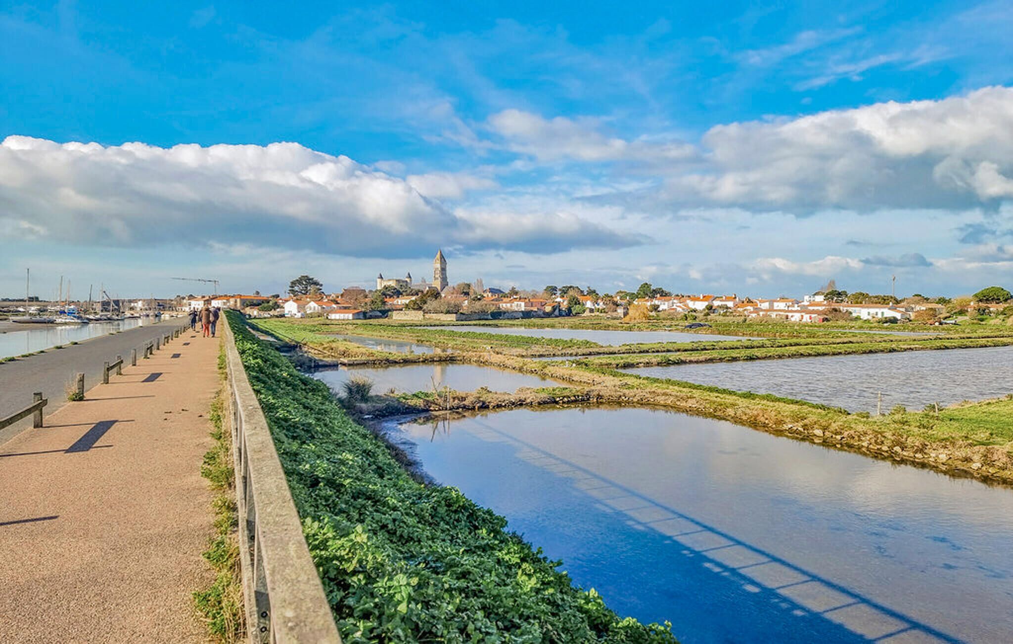 Un paseo fluvial con vista despejada a un pueblo y una torre destacada en la lejanía.