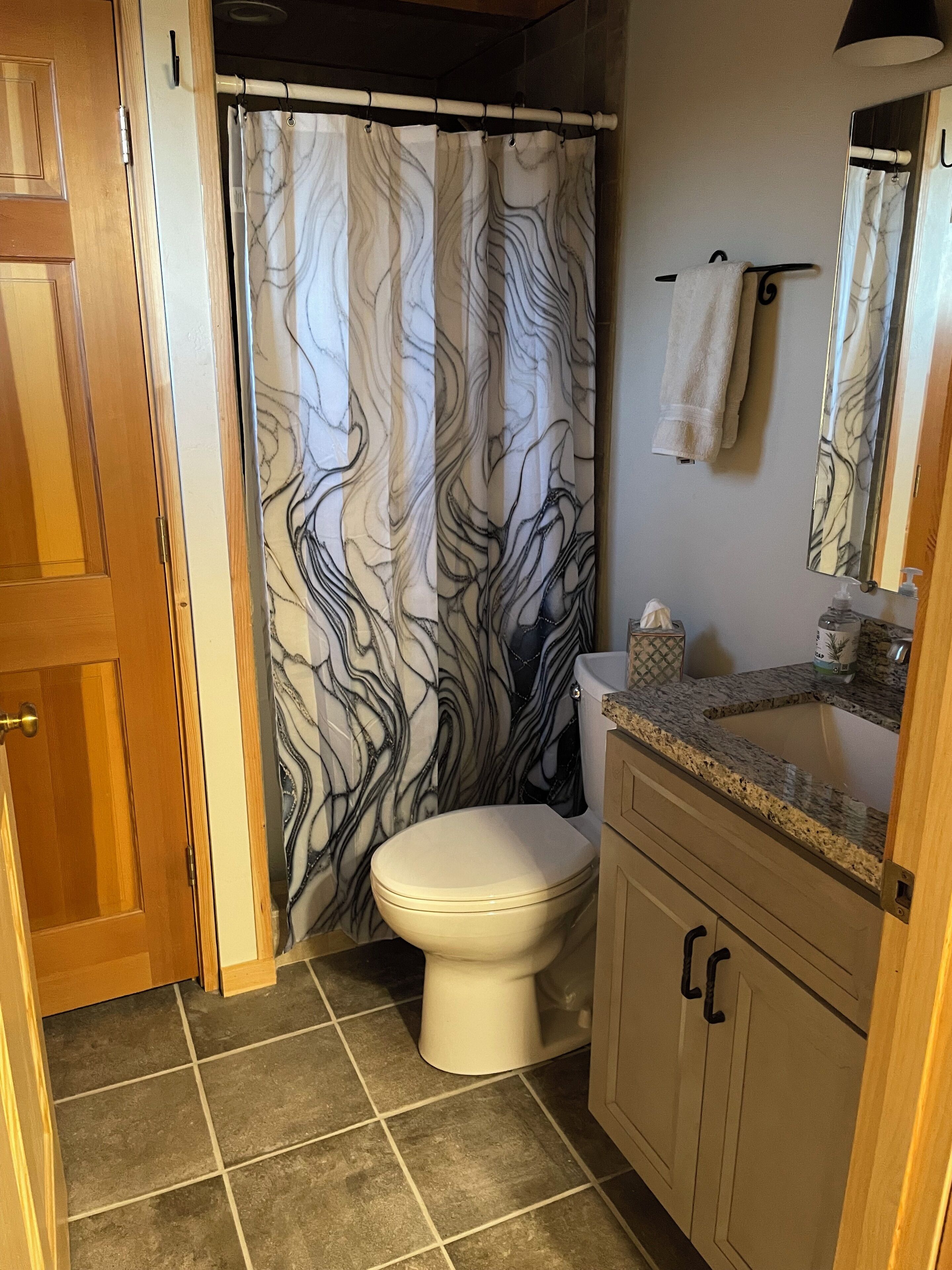 A bathroom with a toilet, a sink with a mirror, and a shower curtain with a marble pattern.
