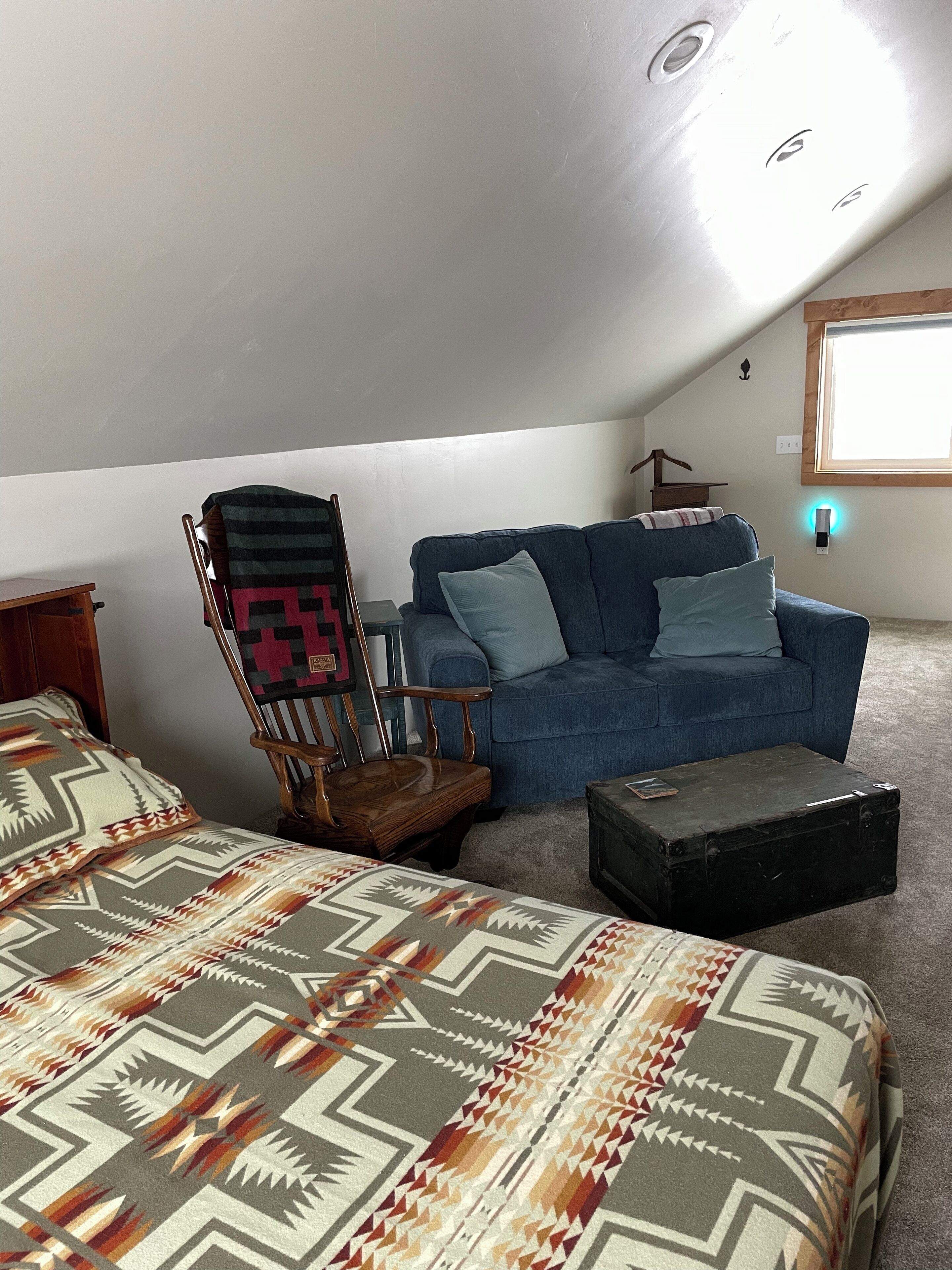 A room with a blue sofa, a wooden chair, a patterned bedspread, and a small black suitcase.