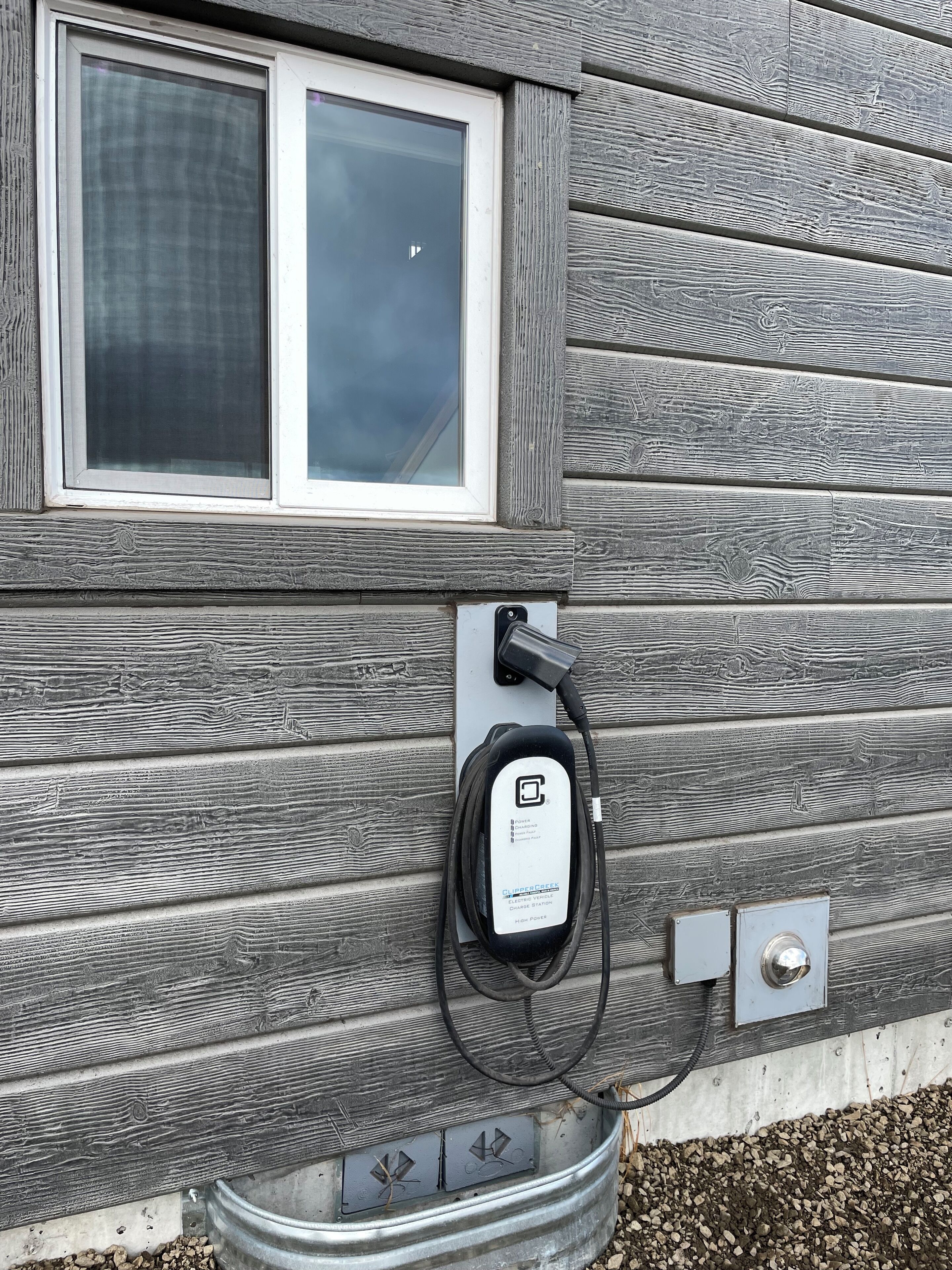 Une borne de recharge pour véhicules électriques, fixée à une maison, avec une fenêtre située juste au-dessus.