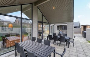 Un espace extérieur aménagé en terrasse, avec une table et des chaises en bois, de grandes portes-fenêtres coulissantes et une vue sur le quartier environnant.