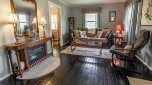 A living room with a dark wooden floor, a sofa, a coffee table, a console table with a mirror, and a chair.