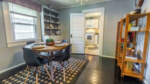 A dining area with a round table, black chairs, a patterned rug, and a bookshelf with various items.