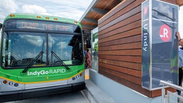 A green public transit bus labeled 'INDYGo RAPID' at a bus stop.