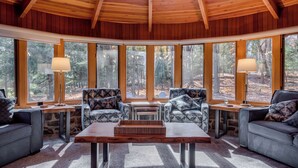 A cozy cabin interior with a wooden ceiling, large windows, and two patterned sofas.