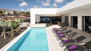 Un espace piscine moderne, doté de chaises longues et d’une piscine.