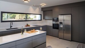 Une cuisine moderne dotée d’un grand îlot central, d’appareils électroménagers en acier inoxydable et d’une fenêtre donnant sur un paysage verdoyant.