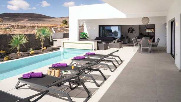 Un espace piscine extérieur moderne, doté de chaises longues et d’un coin repas.