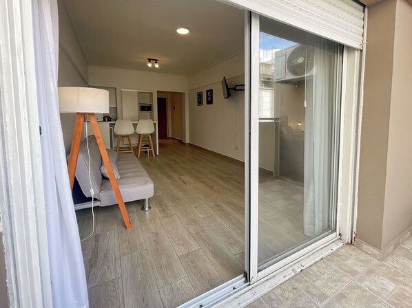Relax in a spacious living area with a sliding glass door leading to a balcony, featuring a comfortable sofa and flat-screen TV.