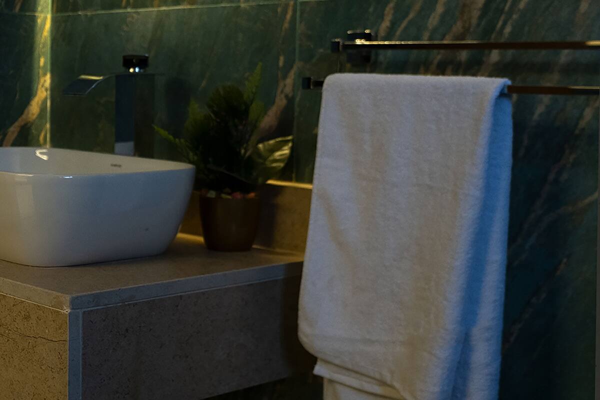 A bathroom with a marble wall, a round mirror, a sink, a towel, and a potted plant.
