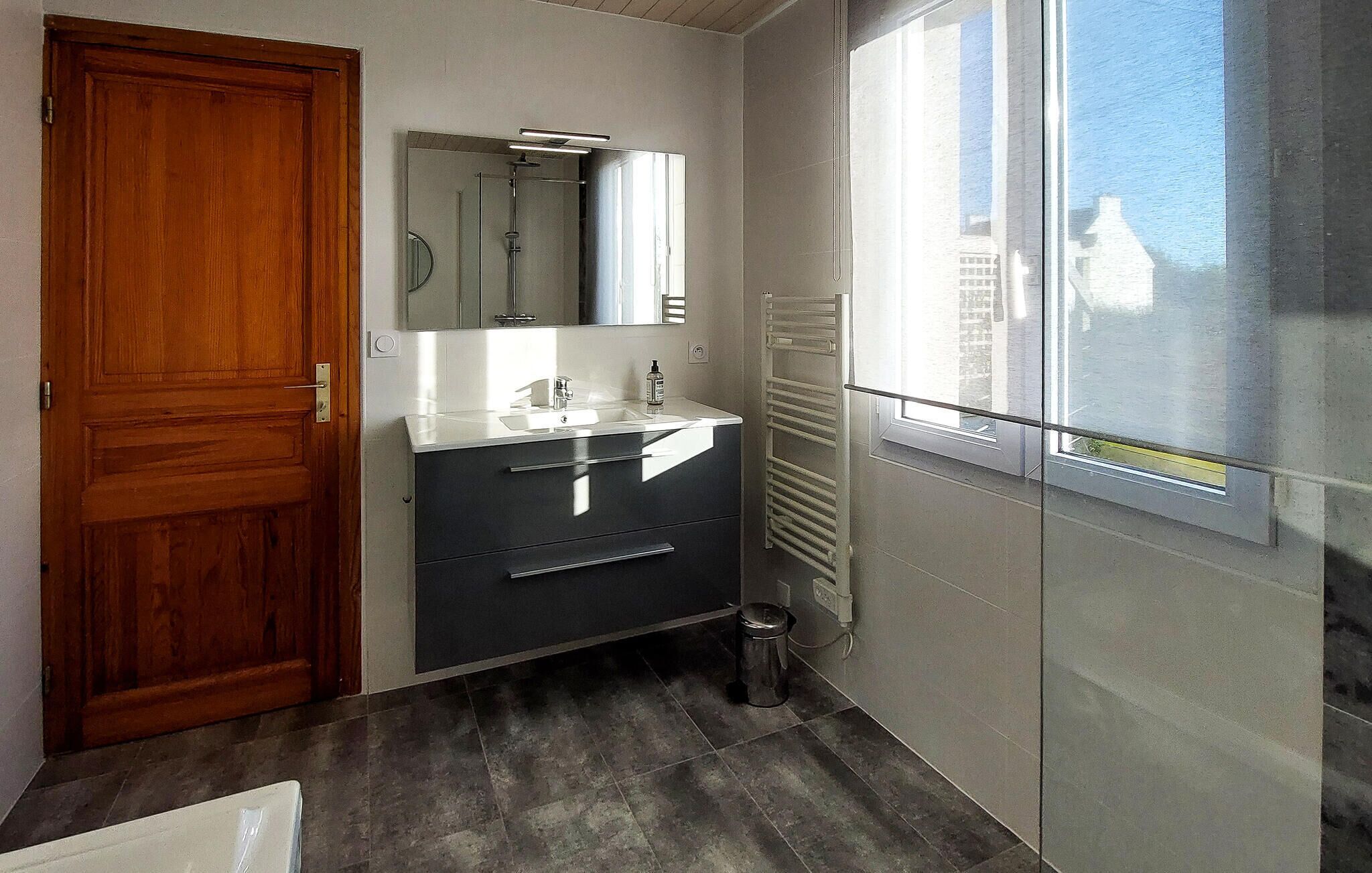 A bathroom with a wooden door, a sink with a mirror, a towel rack, and a window with a view of buildings.