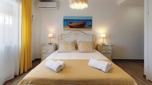 A hotel room with a bed, two bedside tables with lamps, a painting of a boat on the wall, and an air conditioning unit. - Apart. with 4 suites, 10 people with saltwater pool and barbecue in the Algarve (Quarteira)