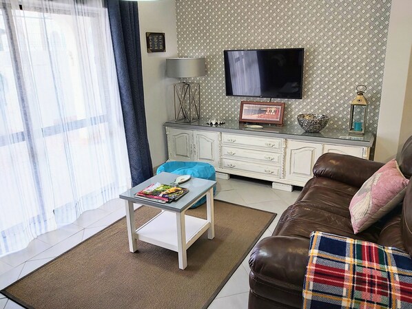 A living room with a sofa, a coffee table, a TV, and a patterned wall.