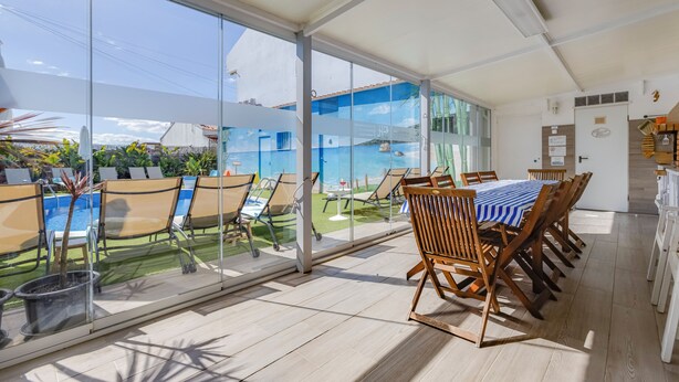 A spacious room with large windows overlooking a pool and garden. There is a dining table with chairs and a small kitchen area. - Apart. with 4 suites, 10 people with saltwater pool and barbecue in the Algarve (Quarteira)