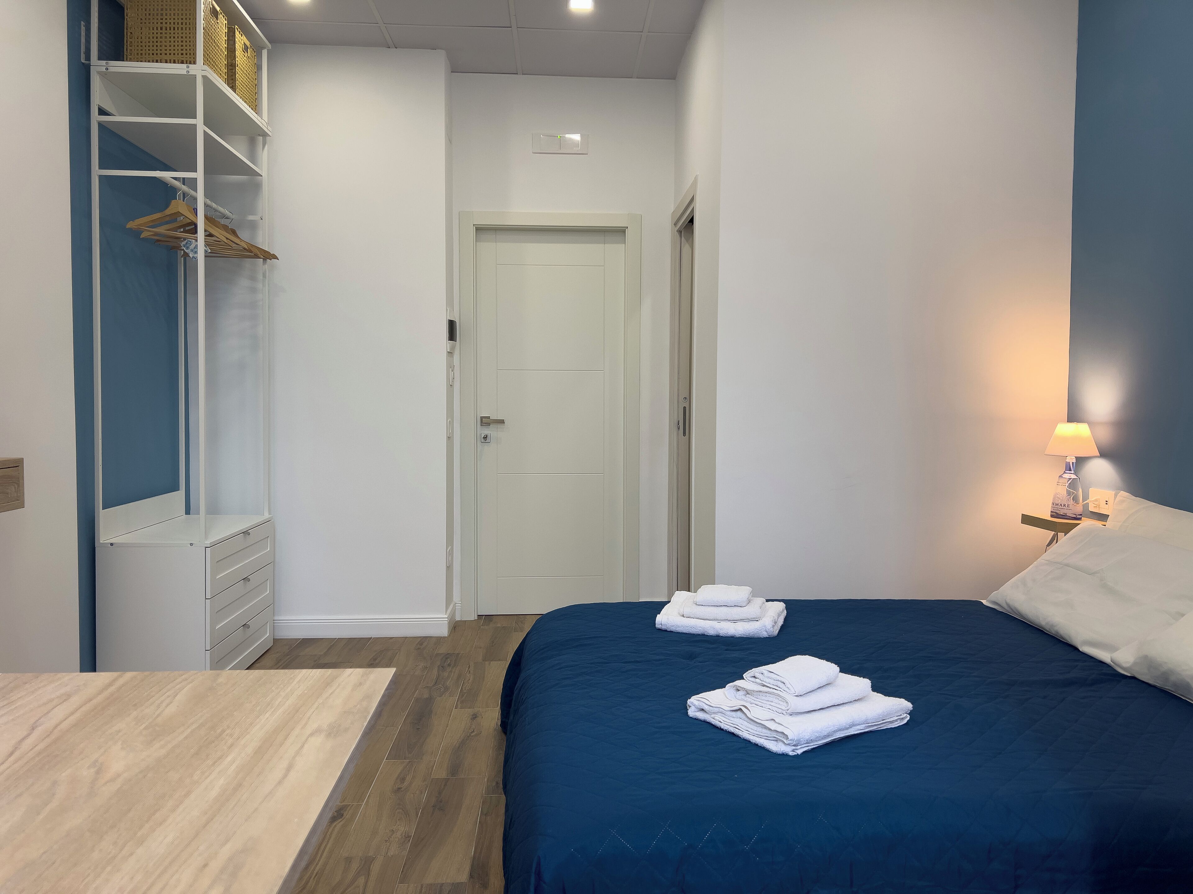 A bedroom with a bed, a nightstand with a lamp, a wardrobe, and a door.