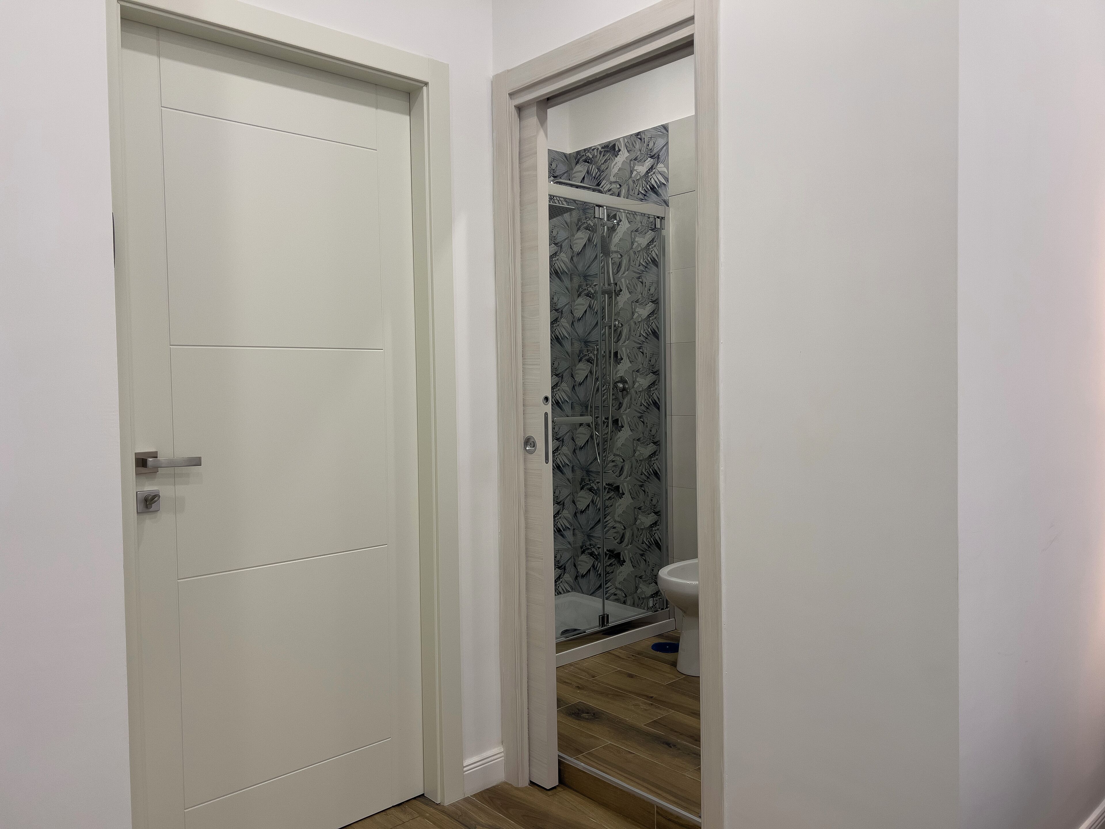 Un bagno con doccia, servizi igienici e una porta che dà su un'altra stanza.