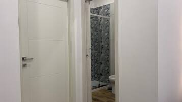 Un bagno con doccia, servizi igienici e una porta che dà su un'altra stanza.