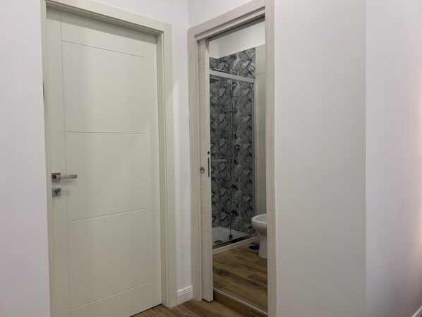 A bathroom with a shower, toilet, and a door leading to another room. - Aura apartments (Naples)