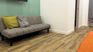 Una habitación con un sofá gris, un cojín verde y suelo de madera.
