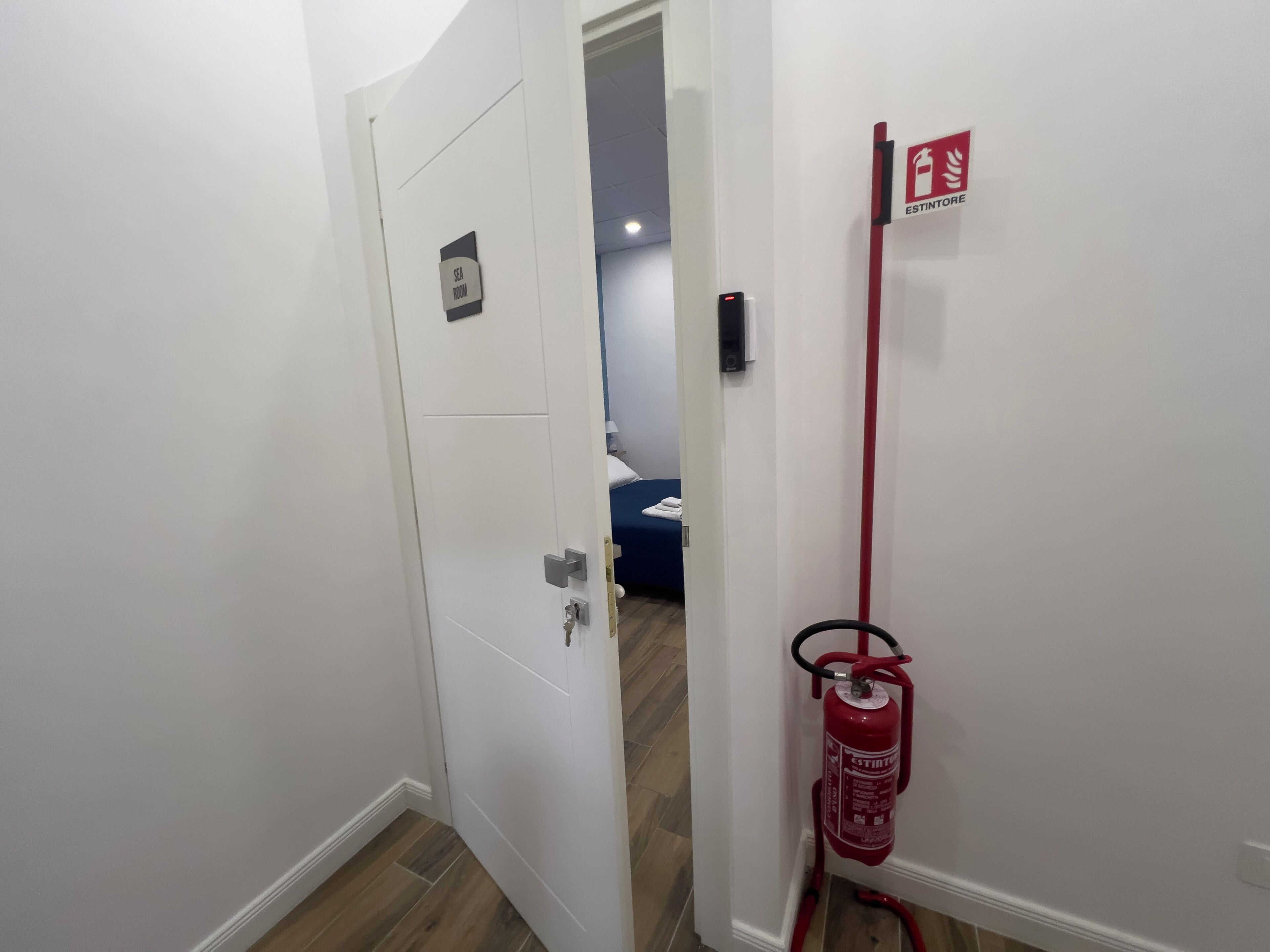 A hallway with a white door labeled "SEA ROOM," a red fire extinguisher mounted on the wall, and a small sign with a flame symbol.