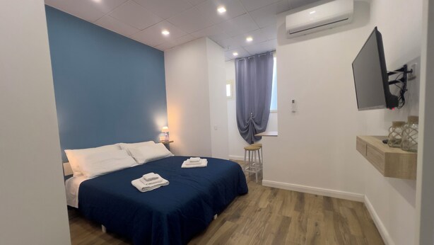 Habitación de hotel con cama, mesita de noche, escritorio, silla, aire acondicionado y televisor de pared.
