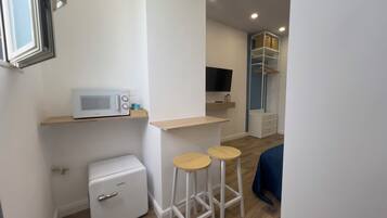 Habitación compacta con microondas, un refrigerador pequeño, televisor y armario con espacio para colgar ropa. Incluye dos taburetes y una mesita.