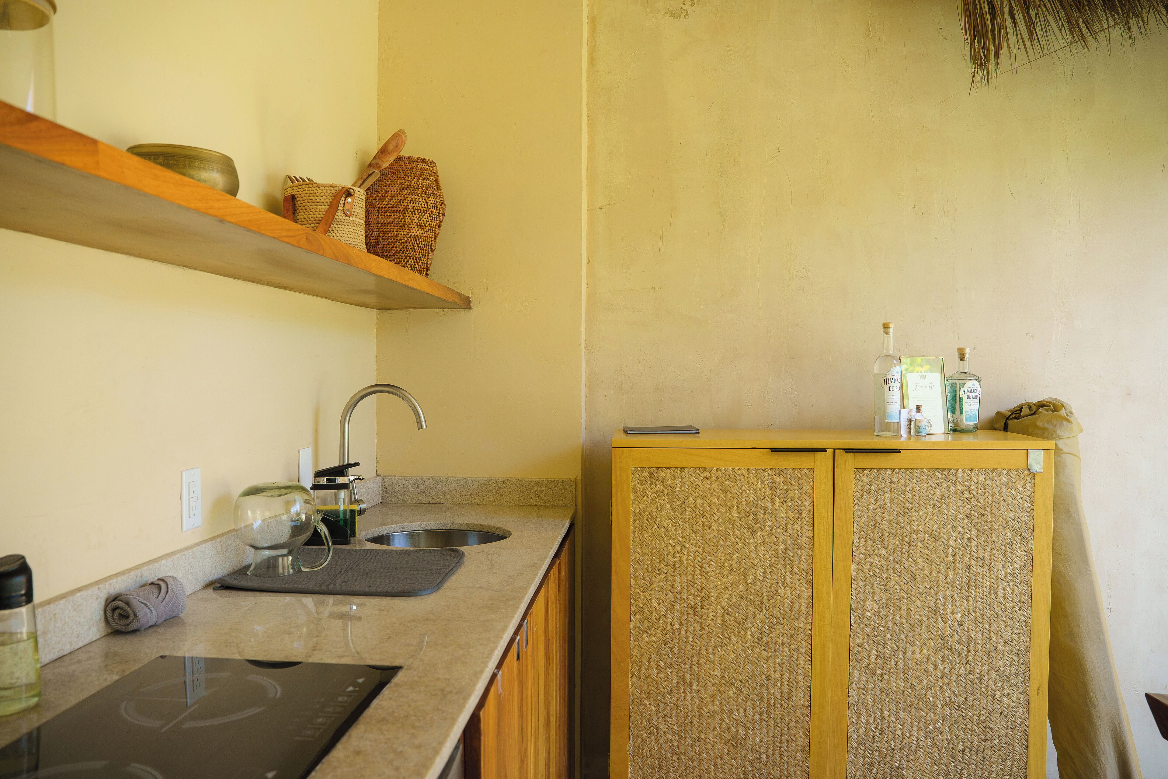 Una cocina con estufa integrada, un lavamanos y un armario de madera con frente tejido.