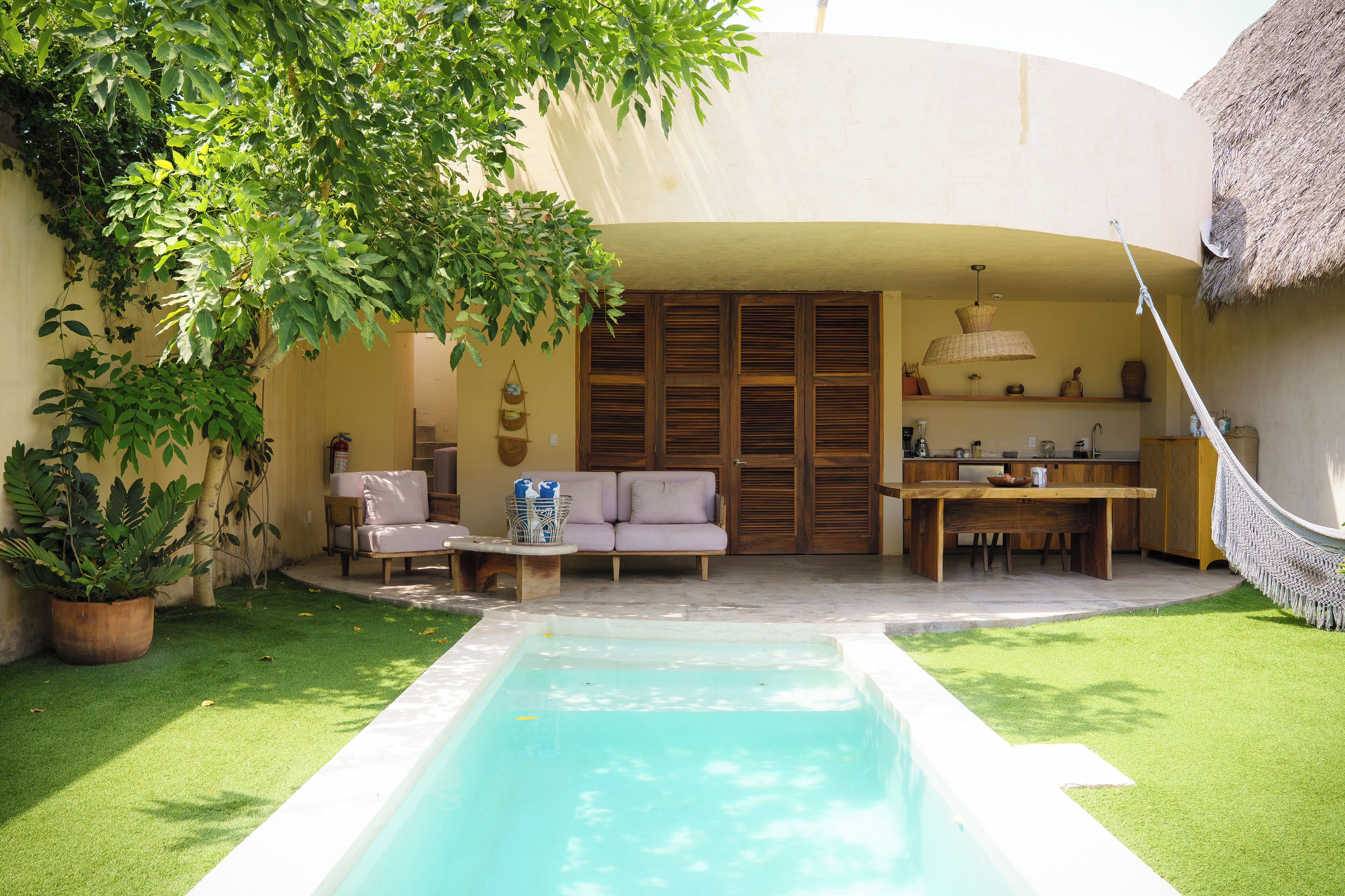 Un área de piscina con mesa y sillas, una hamaca y una estructura de techo de paja.