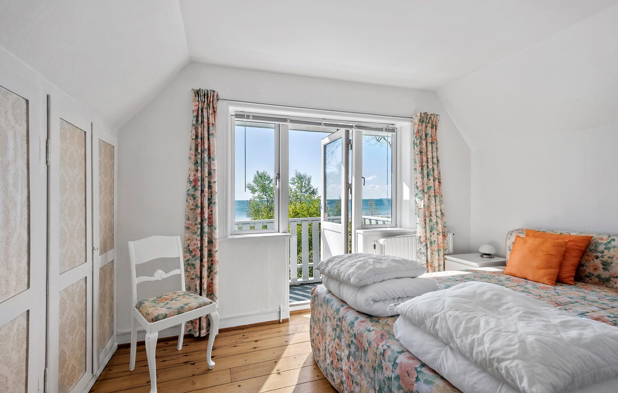 Ein Schlafzimmer mit Bett, Stuhl, einem Fenster mit Vorhängen und Blick ins Freie.