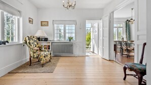 A spacious room with wooden flooring, a radiator, a large window, a chandelier, and a view of the outdoors.