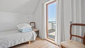 A small, cozy bedroom with a single bed, a chair, and a view of the sea through a sliding glass door.