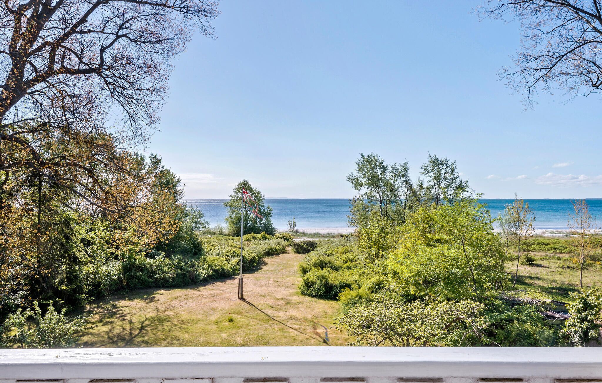 A coastal view with a clear sky, a sandy beach, and dense greenery.