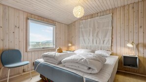 Une chambre à coucher avec un grand lit, une fenêtre, une chaise et une table de chevet avec une lampe.