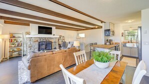 A modern living room with a stone fireplace, a wooden dining table, and a kitchen in the background. - 1 Mi to Skiing: Cozy Townhome in Beech Mountain! (Banner Elk)