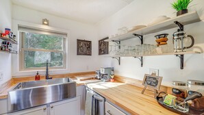 A modern kitchen with a stainless steel sink, wooden countertop, and shelves holding glassware and kitchen items. - 1 Mi to Skiing: Cozy Townhome in Beech Mountain! (Banner Elk)
