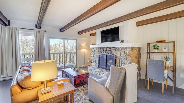 A cozy living room with a stone fireplace, wooden beams, a comfortable sofa, and a television mounted above the fireplace. - 1 Mi to Skiing: Cozy Townhome in Beech Mountain! (Banner Elk)