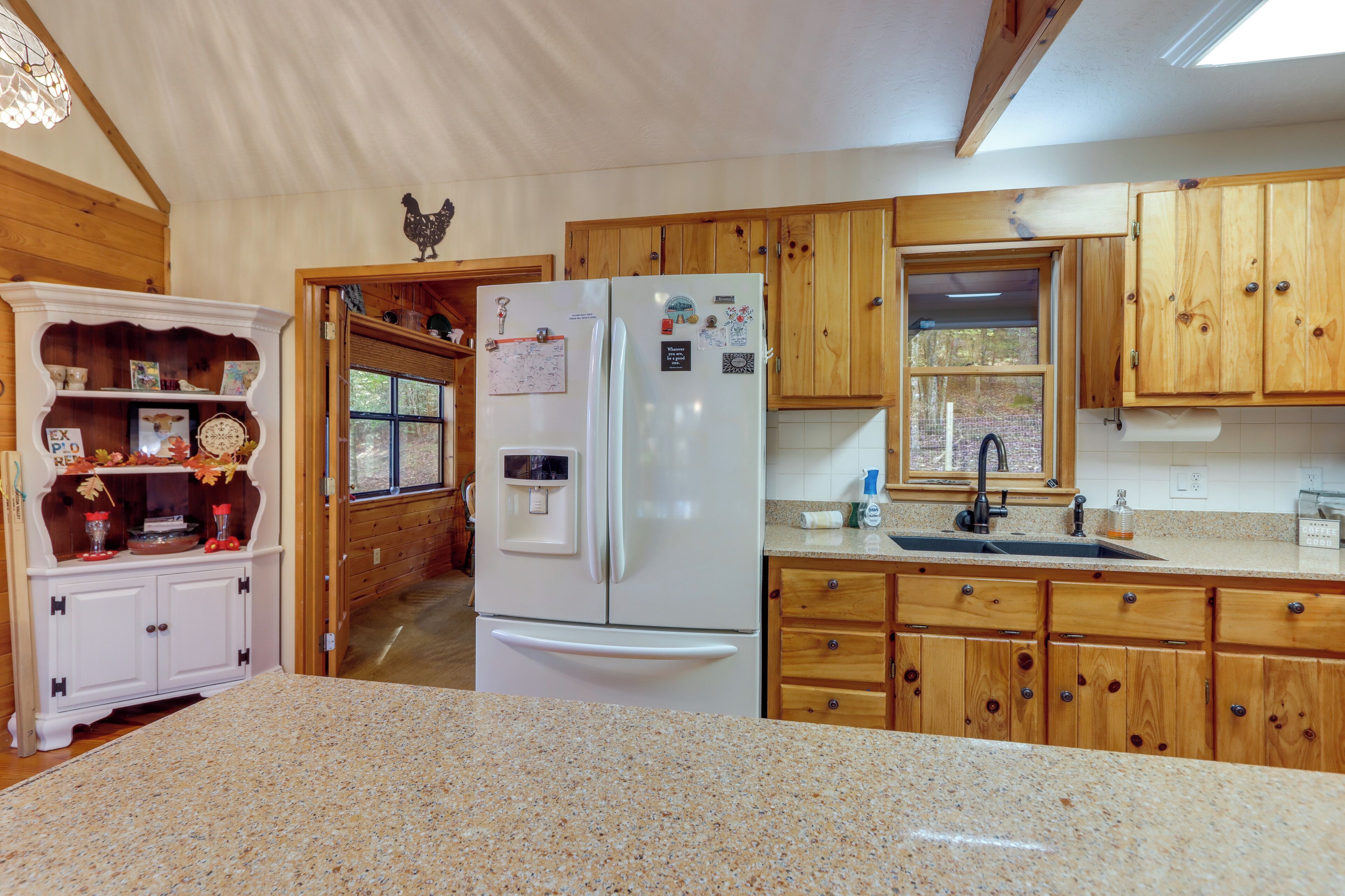 Una cocina con armarios de madera, un refrigerador blanco, encimeras de granito y una ventana con vistas al exterior.