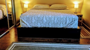 Un dormitorio con una cama grande, dos lámparas de noche, un espejo y suelo de madera.